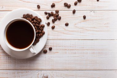 Ahşap bir masa arka plan üzerinde dağınık kahve çekirdekleri ile kahve Fincan. Sonbahar sabah ruh hali, kopya alanı.