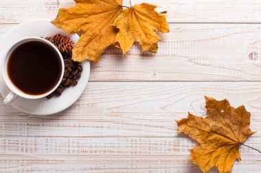 Dağınık kahve çekirdekleri ile kahve fincan, ahşap bir masada kuru sarı yaprakları. Sonbahar sabah ruh hali, kopya alanı.