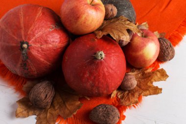 Parlak turuncu sıcak şal, kabak, çilek, elma, fındık ve kuru sarı yaprakları beyaz bir arka plan, sonbahar ruh hali, kopya alanı. Hasat konsepti.