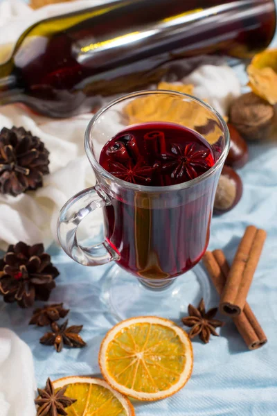 A cup of mulled wine with spices, bottle, dry leaves and oranges on table. Autumn mood, method to keep warm in the cold, copy space, morning light. — Stock Photo, Image