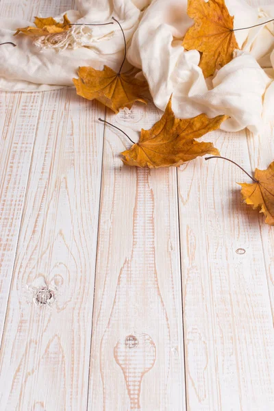 Bufanda blanca y hojas amarillas secas sobre una mesa de madera. Fondo de otoño, espacio de copia . — Foto de Stock