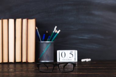 Kitaplar, takvim, defterler, kalemler, bardaklar ve bir fincan kahve, bir karatahtanın arka planında. Öğretmenler Günü için konsept. Boşluğu kopyala.