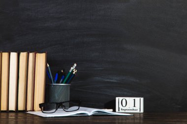 Kitaplar, takvim, defterler, kalemler, bardaklar ve bir fincan kahve, bir karatahtanın arka planında. Bilgi Günü kavramı. Boşluğu kopyala.