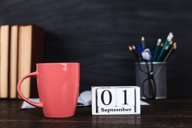 Kitaplar, takvim, defterler, kalemler, bardaklar ve bir fincan kahve, bir karatahtanın arka planında. Öğretmenler Günü için konsept. Boşluğu kopyala.