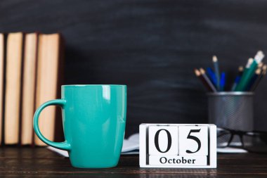 Kitaplar, takvim, defterler, kalemler, bardaklar ve bir fincan kahve, bir karatahtanın arka planında. Öğretmenler Günü için konsept. Boşluğu kopyala.