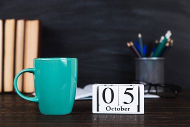 Kitaplar, takvim, defterler, kalemler, bardaklar ve bir fincan kahve, bir karatahtanın arka planında. Öğretmenler Günü için konsept. Boşluğu kopyala.