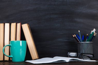 Kitaplar, defterler, kalemler, bardaklar ve bir fincan kahve, bir karatahtanın arka planında. Öğretmenler Günü için kavram.
