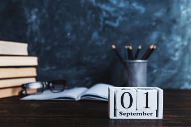 Kitaplar, takvim, defterler, kalemler, bardaklar ve bir fincan kahve, bir karatahtanın arka planında. Bilgi Günü kavramı. Boşluğu kopyala.