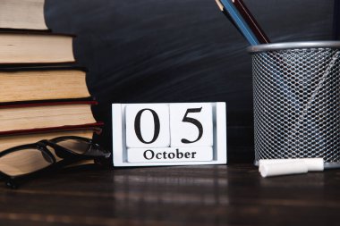 Kitaplar, takvim, defterler, kalemler, bardaklar ve bir fincan kahve, bir karatahtanın arka planında. Öğretmenler Günü için konsept. Boşluğu kopyala.