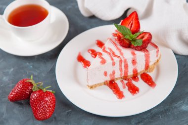 Tatlı kahvaltı, çay ve taze çilek ve nane aromalı lezzetli cheesecake, pişirilmemiş ev yapımı tarif, koyu mavi taş masa. Boşluğu kopyala.
