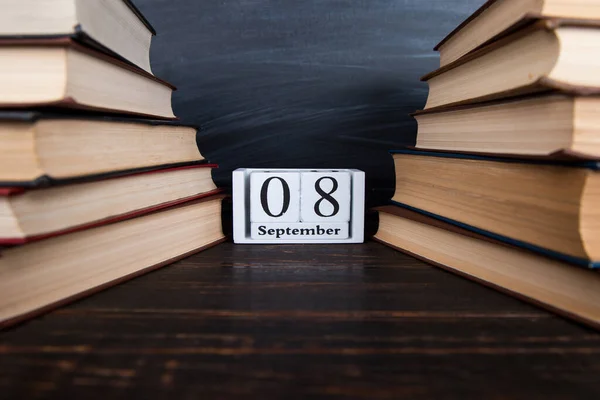 Calendar among books against the background of the chalk board. Concept for Knowledge Day, beginning of the school year.