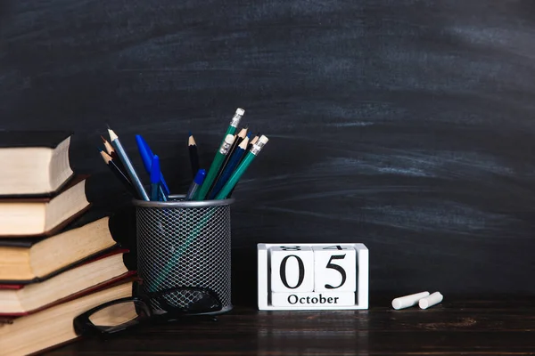 Books, calendar, notebooks, pencils, glasses and a cup of coffee, against the background of a chalkboard. Concept for Teacher\'s Day. Copy space.
