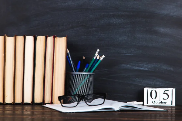 Books, calendar, notebooks, pencils, glasses and a cup of coffee, against the background of a chalkboard. Concept for Teacher's Day. Copy space.