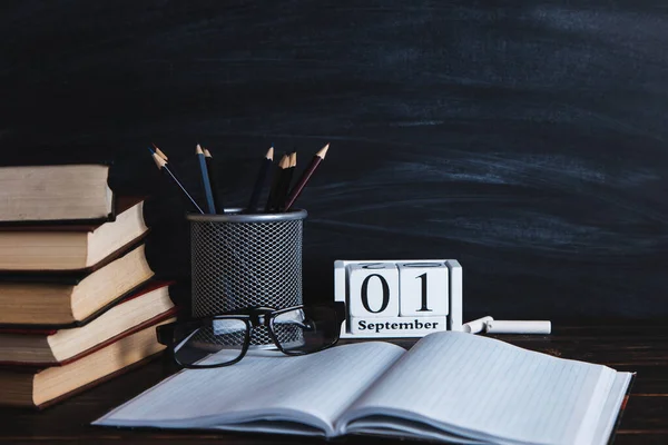 Books, calendar, notebooks, pencils, glasses and cup of coffee, against the background of a chalkboard. Concept for knowledge day. Copy space.