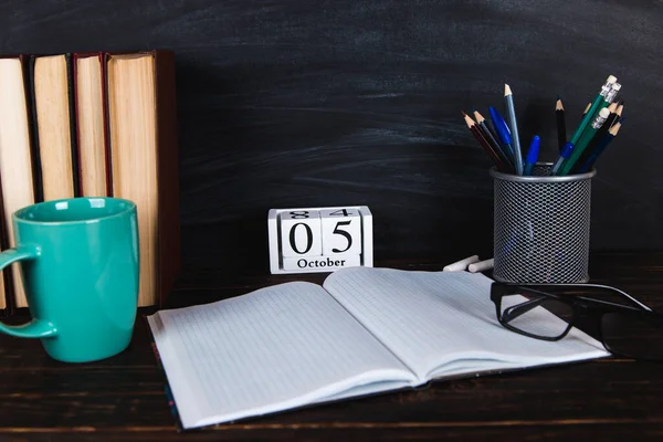 Books, calendar, notebooks, pencils, glasses and a cup of coffee, against the background of a chalkboard. Concept for Teacher\'s Day. Copy space.