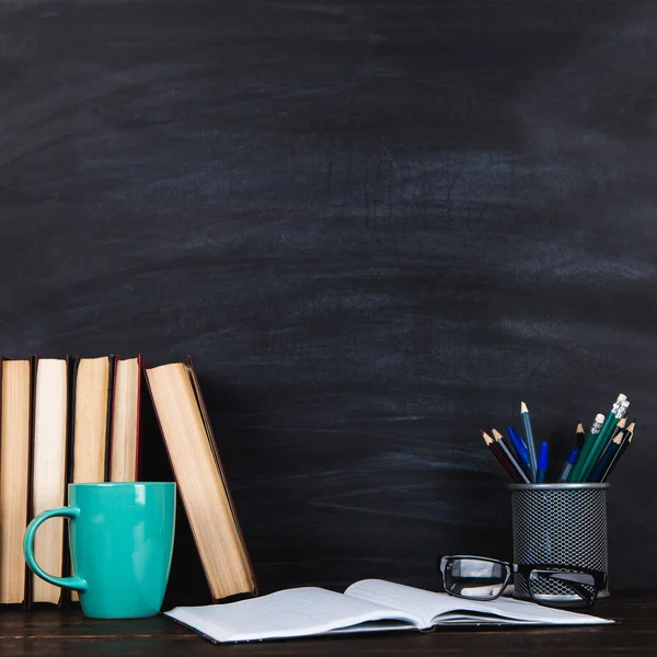 Books, notebooks, pencils, glasses and a cup of coffee, against the background of a chalkboard. Concept for Teacher\'s Day.