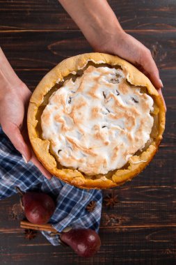 Kadın ellerinde kremalı armut turtası, ahşap masada ev yapımı pastalar, baharatlar. Boşluğu kopyala.