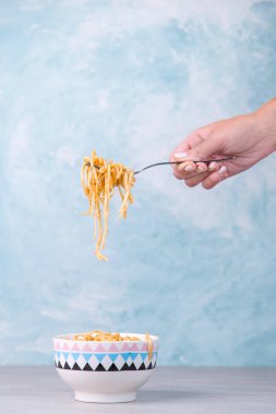 Renkli kasede soslu şehriyeler, sallanan bir çatal makarna, mavi arka planda iştah spagettisi..