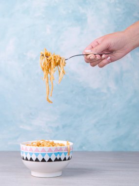 Renkli kasede soslu şehriyeler, sallanan bir çatal makarna, mavi arka planda iştah spagettisi..