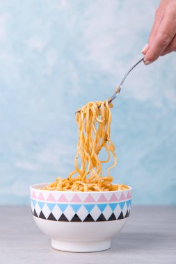 Renkli kasede soslu şehriyeler, sallanan bir çatal makarna, mavi arka planda iştah spagettisi..