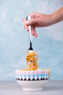 Renkli kasede soslu şehriyeler, sallanan bir çatal makarna, mavi arka planda iştah spagettisi..