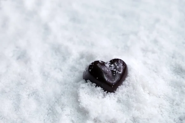Assorted milk and dark chocolate heart on snow with copy space, Black Valentine\'s Day concept.