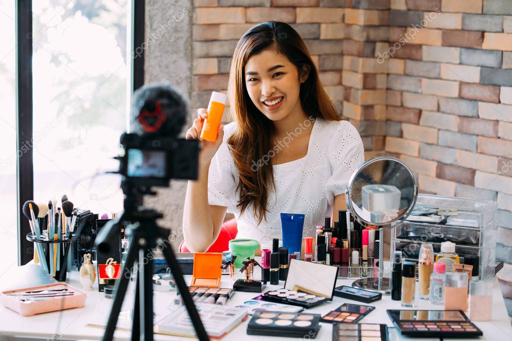 Charming Asian girl recording vlog. Beauty blogger presenting makeup cosmetics in front of camera