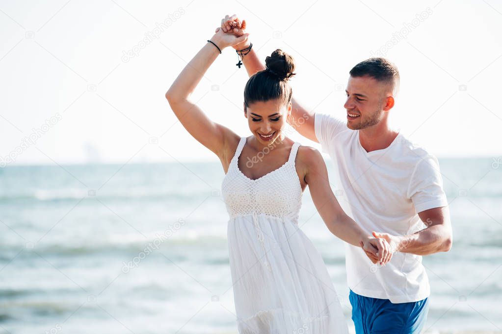 Young happy and joyful Caucasian adult romantic couple dancing on the tropical summer beach - honeymoon travel and leisure concept