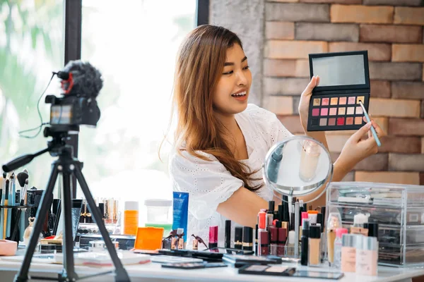 Mujer bastante asiática grabando vídeo tutorial de maquillaje sobre cosméticos con teléfono móvil en trípode — Foto de Stock