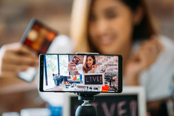 Улыбающаяся азиатка показывает тени для век на дисплее смартфона — стоковое фото