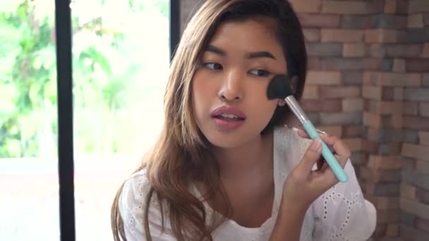 Joven asiática sonriente mujer usando maquillaje cepillos y mirando a la cámara en casa . — Vídeos de Stock