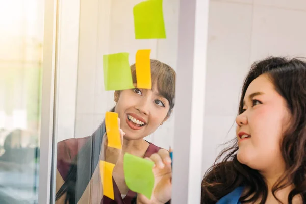 Colleghi sorridenti che prendono appunti sugli adesivi su vetro — Foto Stock