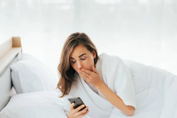 Verblüffte Frau blickt auf Smartphone im Bett — Stockfoto