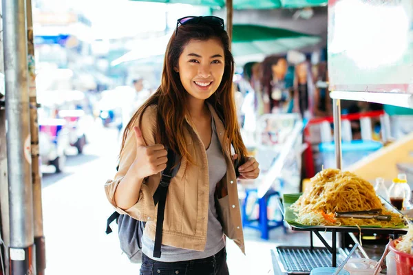 ストリートフード屋台の前で親指アップジェスチャーを与えて若いアジアの女性 — ストック写真