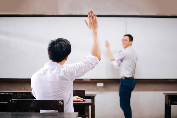 年轻的成年男生举起手来向另一位男老师提问. — 图库照片