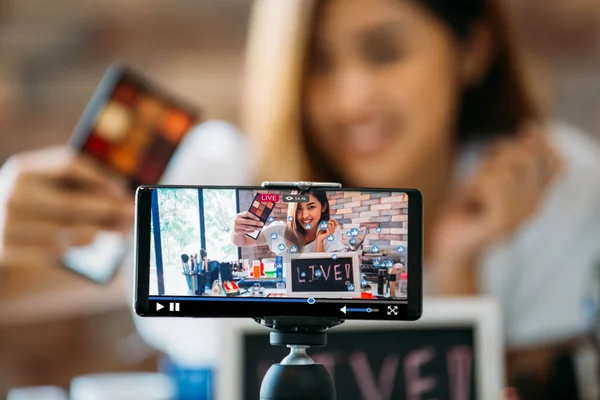 Улыбающаяся азиатка показывает тени для век на дисплее смартфона — стоковое фото