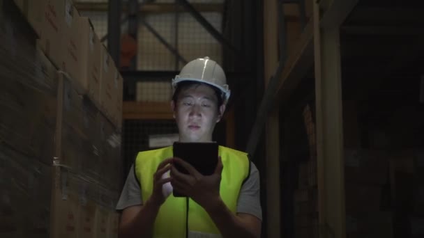 Jeune ouvrier d'entrepôt avec un casque de sécurité marche avec une tablette numérique dans la salle d'inventaire 