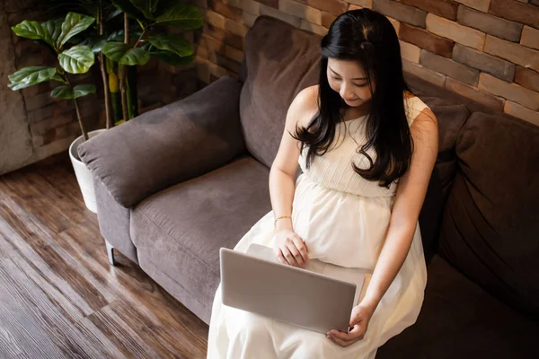 Беременная азиатка дома с ноутбуком — стоковое фото