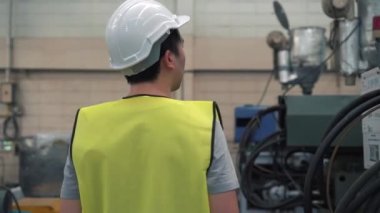 Genç sanayi mühendisi fabrika tesislerinde yürüyor ve üretim makinelerini kontrol ediyor.