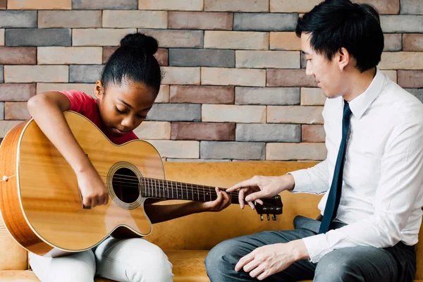 Joven profesor asiático dando una lección de guitarra y enseñando a tocar la guitarra a chica afroamericana —  Fotos de Stock