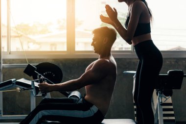 Spor salonundaki genç beyaz adam, sıkı çalışıyor ve kablolu yayında ağırlık kaldırıyor.