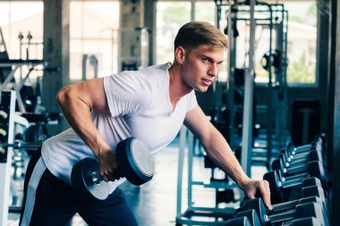Spor salonunda beyaz gömlekli genç beyaz bir adam, rahatlamak için halterleri kaldırıyor.