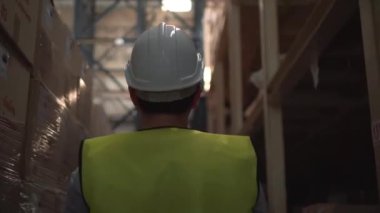 Güvenlik kasketi olan genç bir depo çalışanı envanter odasında yürüyor.