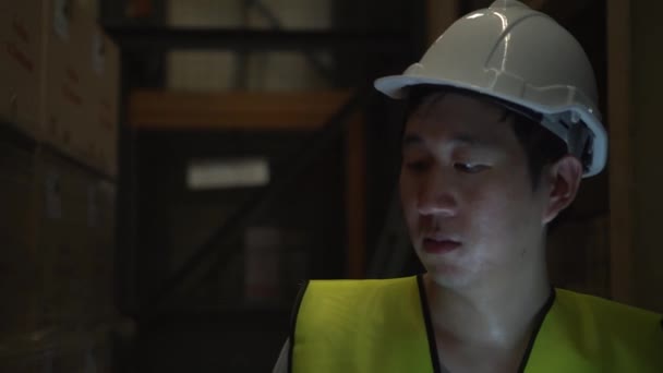 Young warehouse worker with safety hard hat is walking with a digital tablet through inventory room — 비디오