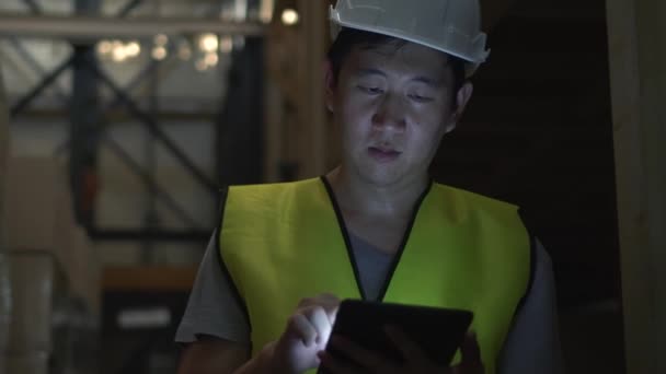 Joven trabajador de almacén con sombrero duro de seguridad está comprobando los detalles de la orden con una tableta digital en la sala de inventario — Vídeos de Stock