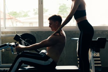 Spor salonundaki genç beyaz adam, sıkı çalışıyor ve kablolu yayında ağırlık kaldırıyor.