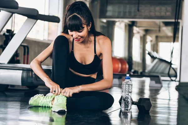 Young happy Caucasian sporty woman tying shoelace on green shoes in gym — Stock Photo, Image