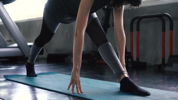 Молодая белая женщина растягивает ноги на полу спортзала. Девочка в форме, которая занимается разминкой и тренировкой — стоковое видео