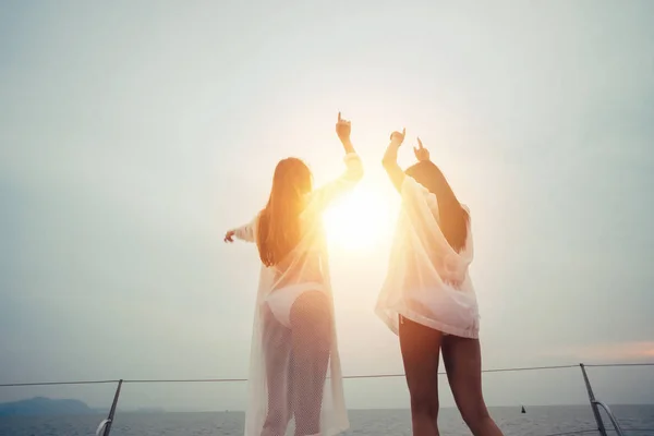 Jovem duas amigas levantando as mãos usando biquíni de verão contra a luz do sol — Fotografia de Stock