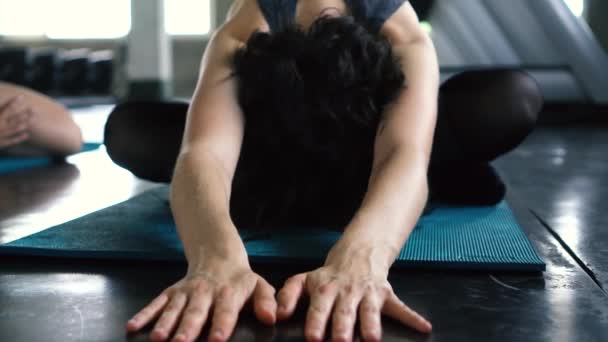 Joven atractiva mujer caucásica estirando sus piernas en el piso del gimnasio y sonriendo a la cámara — Vídeos de Stock